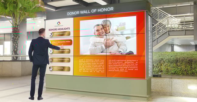 A man standing in front of a donor wall focusing on donor highlights.